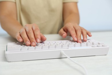 Photo of Woman typing on modern keyboard with RGB lighting at white wooden table, closeup