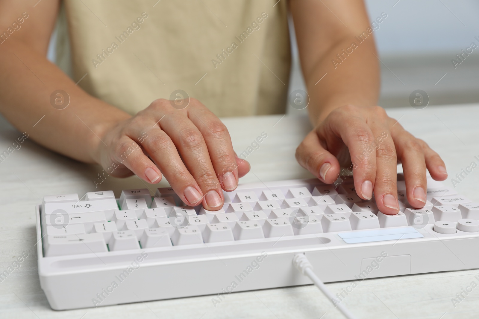Woman typing on modern keyboard with RGB lighting at white wooden table, closeup Photo of Woman typing on modern keyboard with RGB lighting at white wooden table, closeup