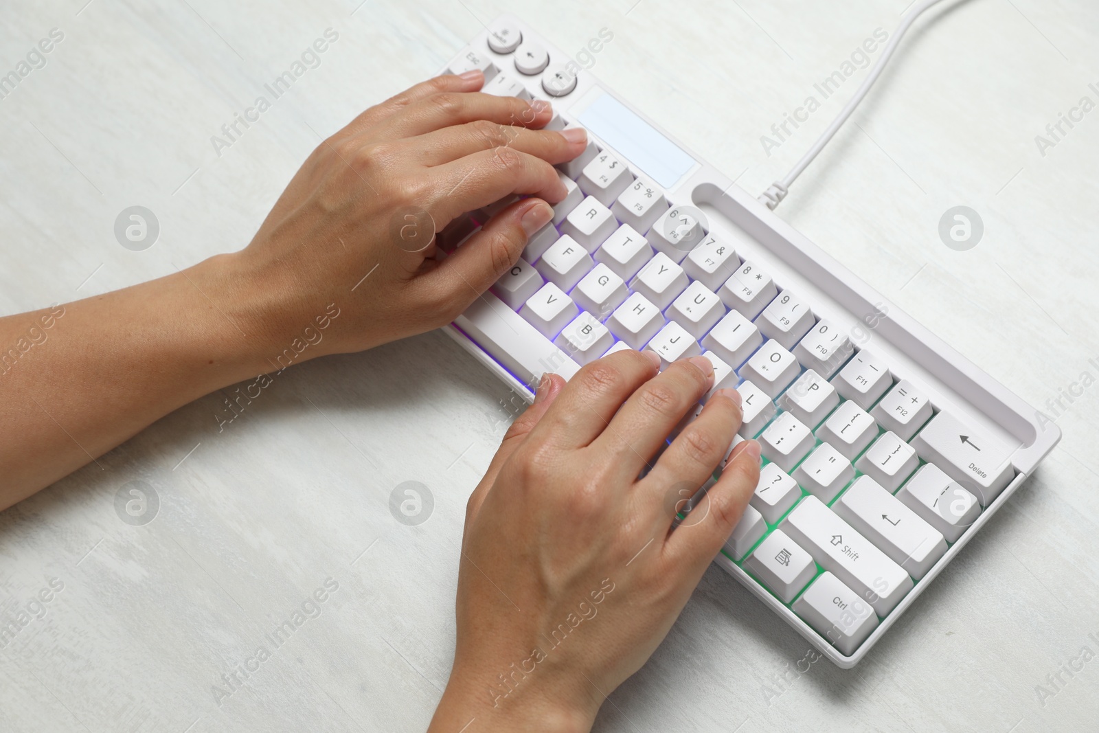 Woman typing on modern keyboard with RGB lighting at white wooden table, above view Photo of Woman typing on modern keyboard with RGB lighting at white wooden table, above view