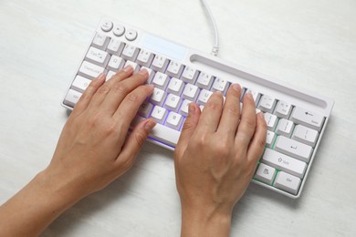 Photo of Woman typing on modern keyboard with RGB lighting at white wooden table, above view
