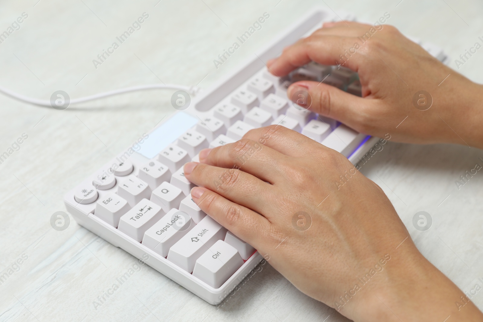 Woman typing on modern keyboard with RGB lighting at white wooden table, closeup Photo of Woman typing on modern keyboard with RGB lighting at white wooden table, closeup