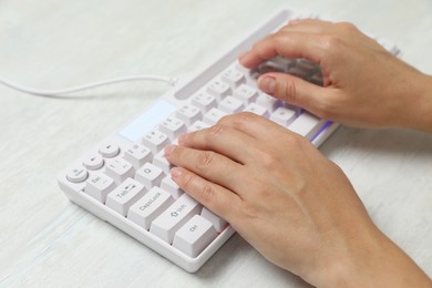 Photo of Woman typing on modern keyboard with RGB lighting at white wooden table, closeup
