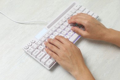 Photo of Woman typing on modern keyboard with RGB lighting at white wooden table, closeup