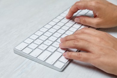 Photo of Woman typing on wireless keyboard at white wooden table, closeup