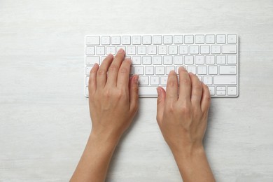 Photo of Woman typing on wireless keyboard at white wooden table, top view