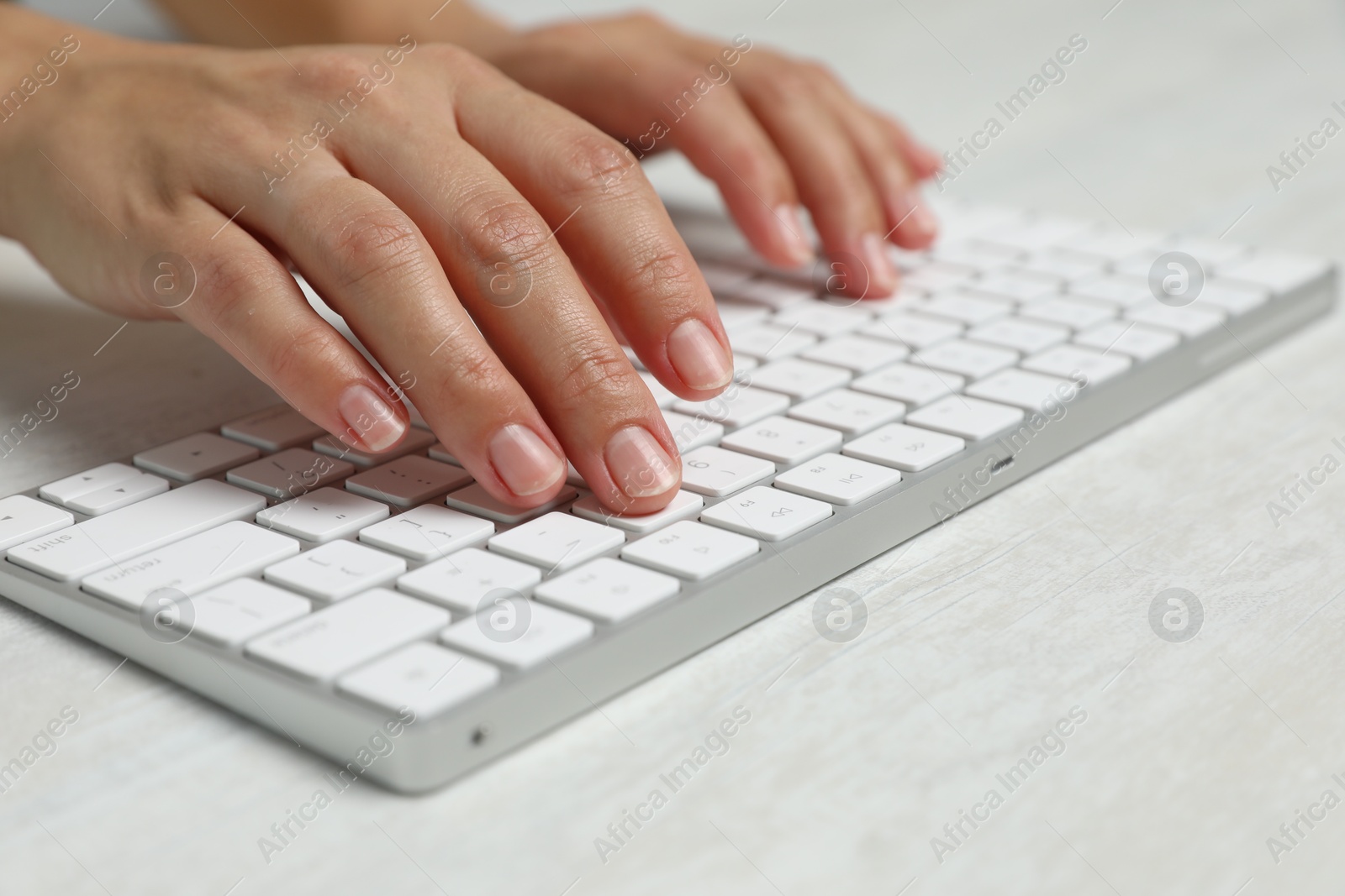 Woman typing on wireless keyboard at white wooden table, closeup Photo of Woman typing on wireless keyboard at white wooden table, closeup