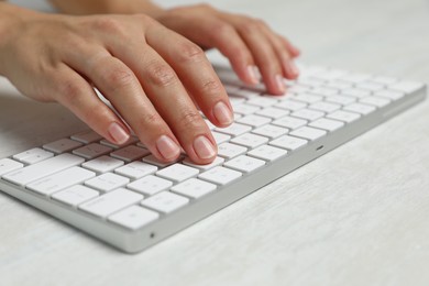 Photo of Woman typing on wireless keyboard at white wooden table, closeup