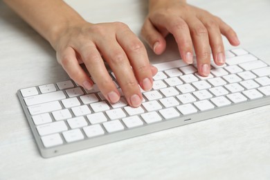 Photo of Woman typing on wireless keyboard at white wooden table, closeup