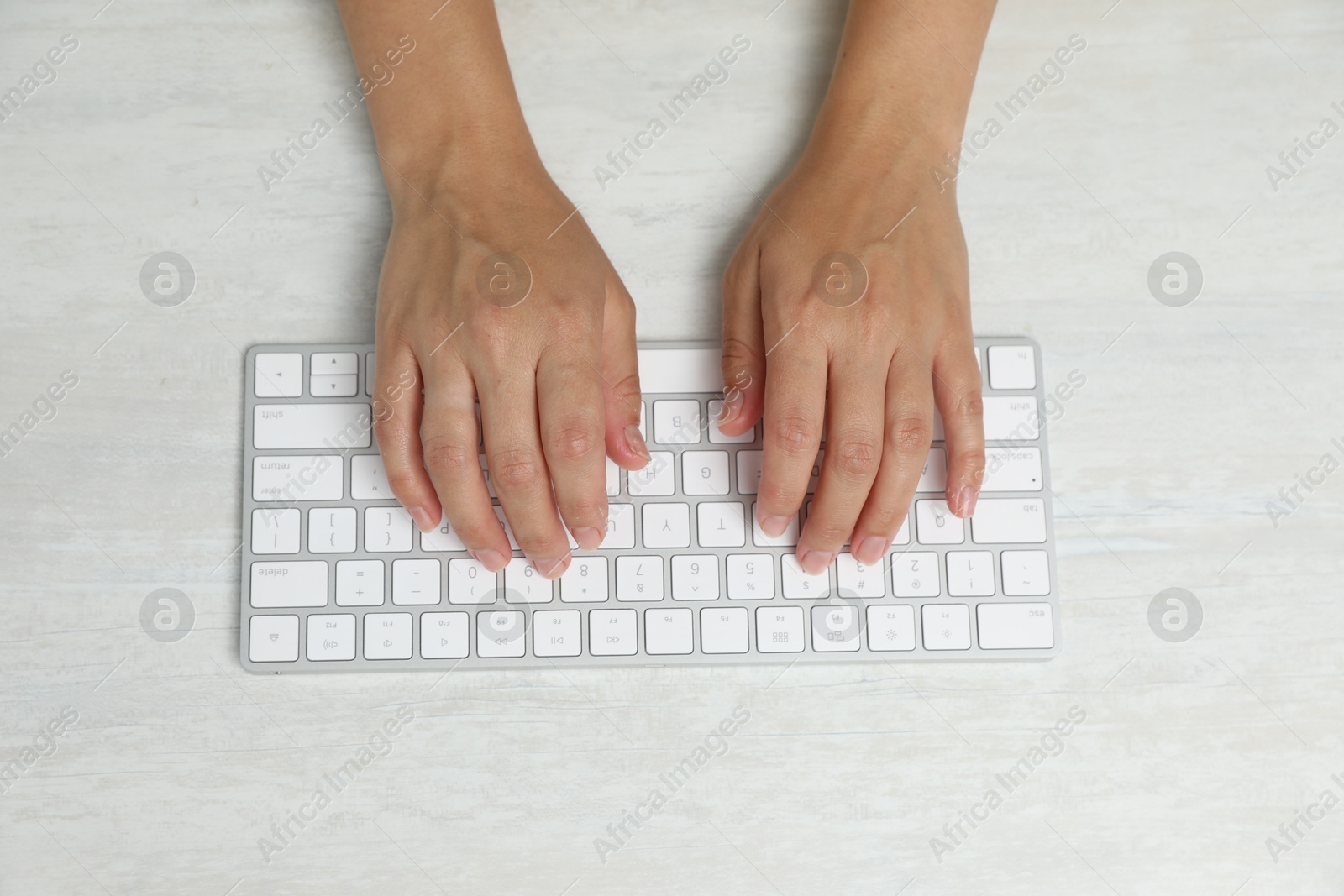 Photo of Woman typing on wireless keyboard at white wooden table, top view
