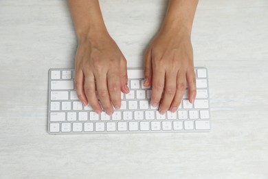 Photo of Woman typing on wireless keyboard at white wooden table, top view