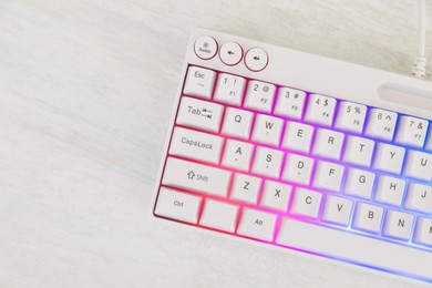 Photo of Modern keyboard with RGB lighting on white wooden table, top view. Space for text
