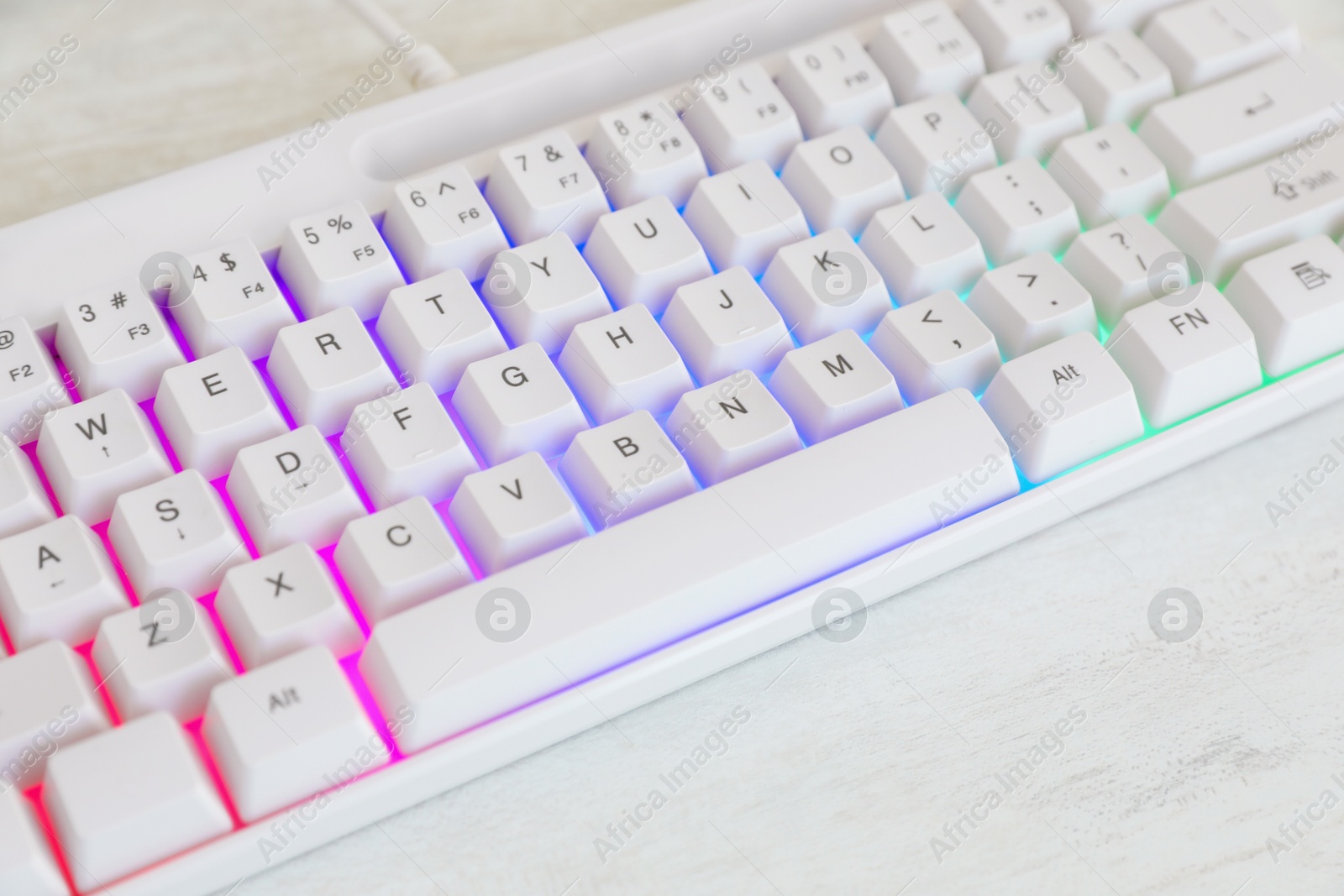 Photo of Modern keyboard with RGB lighting on white wooden table, closeup