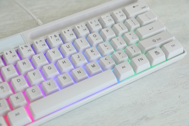 Photo of Modern keyboard with RGB lighting on white wooden table, closeup