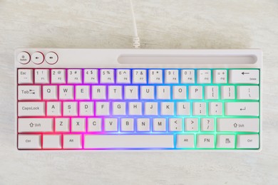 Photo of Modern keyboard with RGB lighting on white wooden table, top view