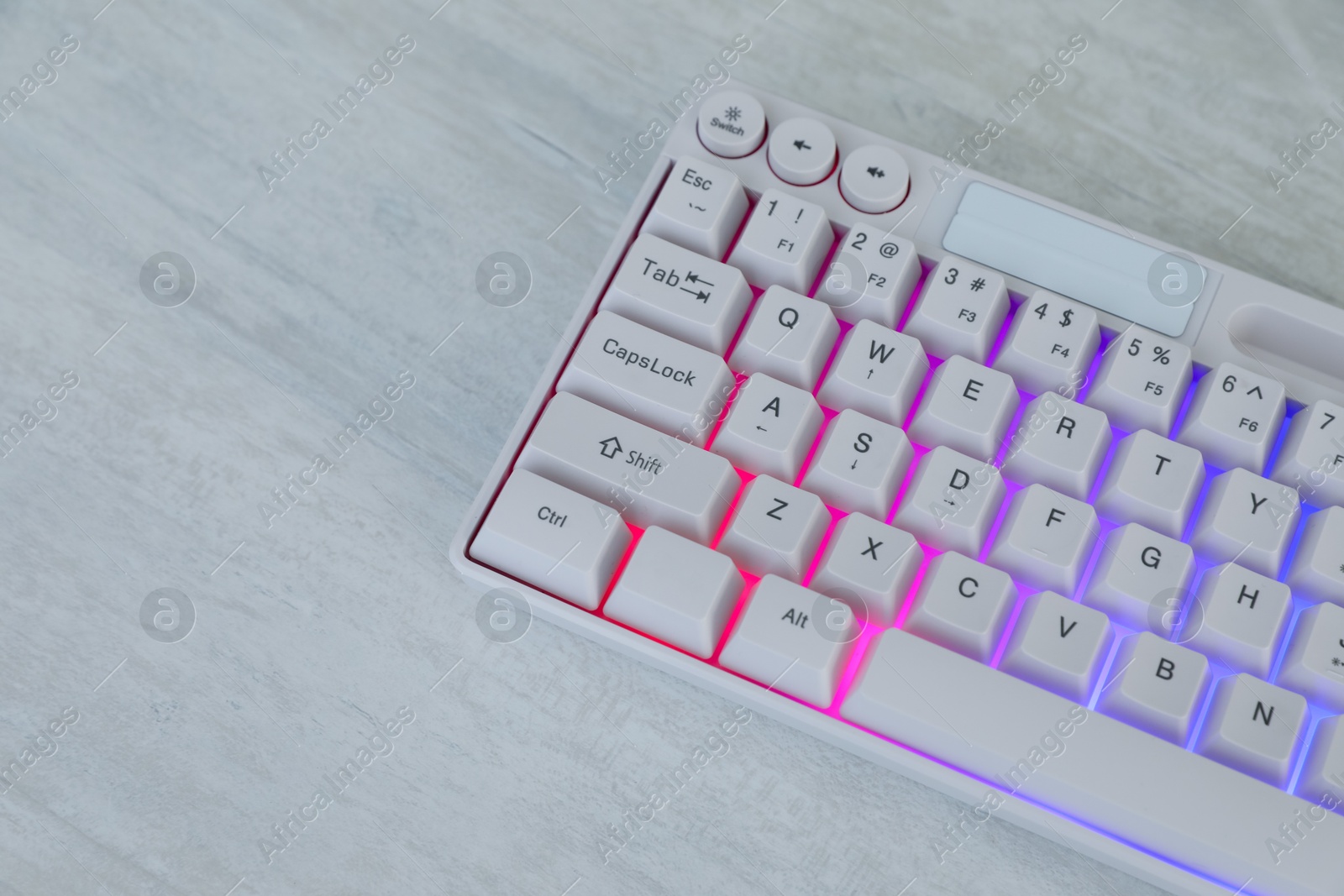 Photo of Modern keyboard with RGB lighting on white wooden table, closeup. Space for text