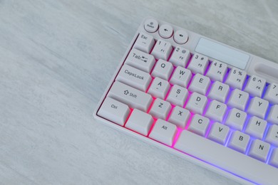 Photo of Modern keyboard with RGB lighting on white wooden table, closeup. Space for text