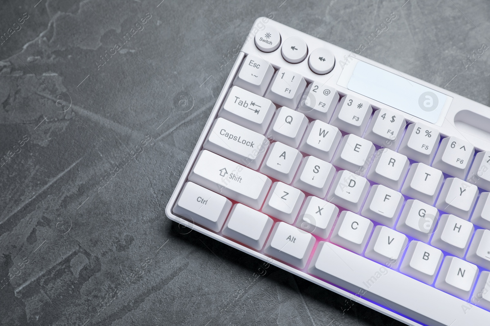 Photo of Modern white keyboard with RGB lighting on grey table, above view. Space for text