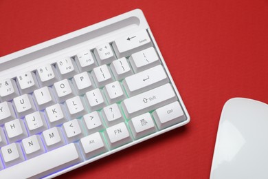 Photo of Modern white keyboard with RGB lighting and mouse on red background, above view