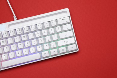 Photo of Modern white keyboard with RGB lighting on red background, top view. Space for text