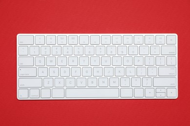 Photo of Modern white wireless keyboard on red background, top view