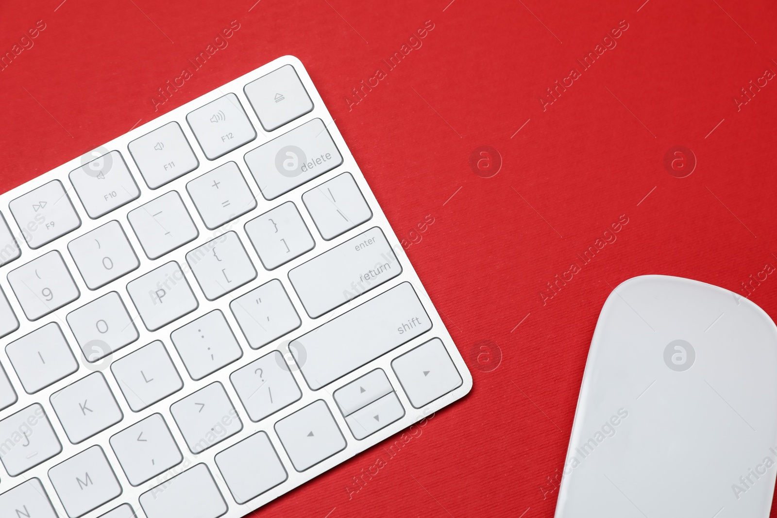 Modern white wireless keyboard and mouse on red background, top view Photo of Modern white wireless keyboard and mouse on red background, top view
