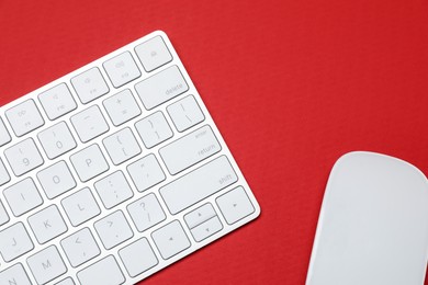 Photo of Modern white wireless keyboard and mouse on red background, top view