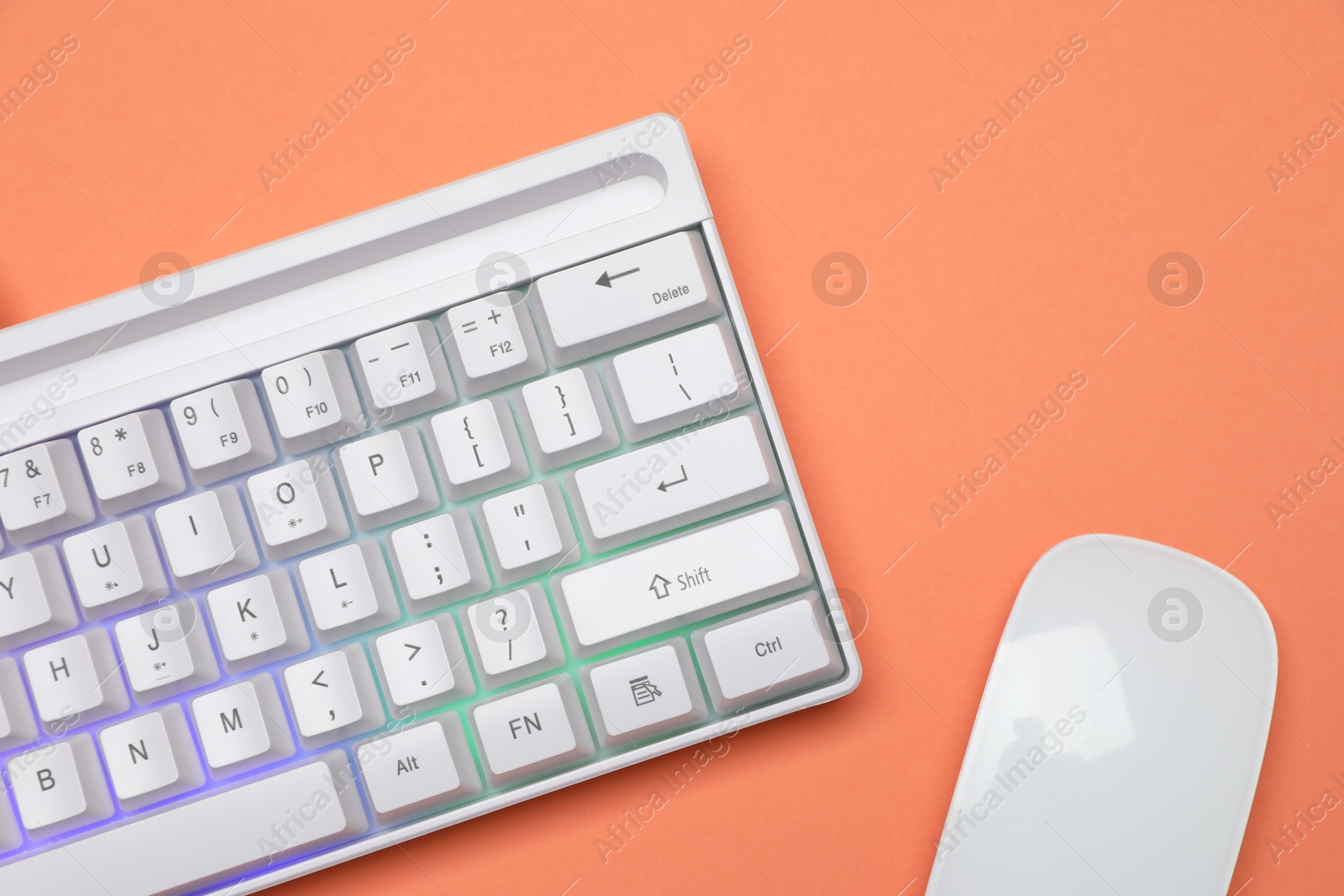 Modern white keyboard with RGB lighting and mouse on orange background, top view Photo of Modern white keyboard with RGB lighting and mouse on orange background, top view