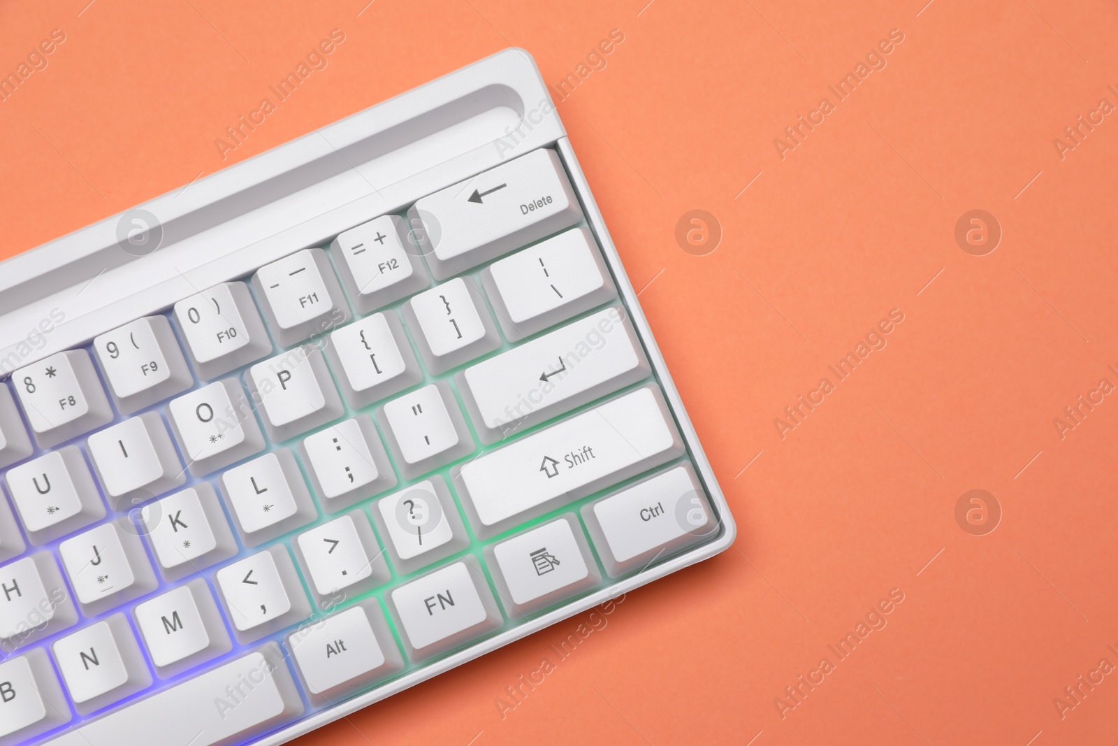 Photo of Modern white keyboard with RGB lighting on orange background, top view. Space for text