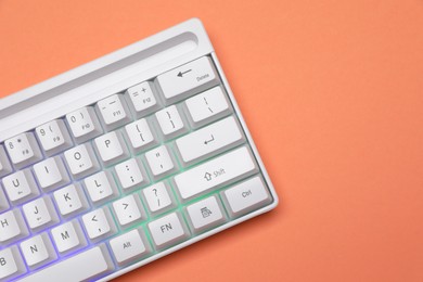 Photo of Modern white keyboard with RGB lighting on orange background, top view. Space for text