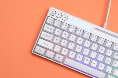 Photo of Modern white keyboard with RGB lighting on orange background, top view. Space for text