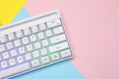 Photo of Modern white keyboard with RGB lighting on color background, top view. Space for text