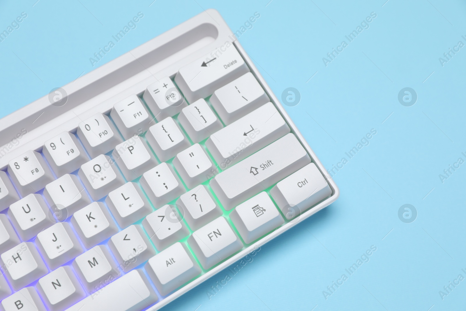 Modern white keyboard with RGB lighting on light blue background, closeup. Space for text Photo of Modern white keyboard with RGB lighting on light blue background, closeup. Space for text