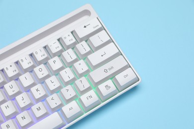 Photo of Modern white keyboard with RGB lighting on light blue background, closeup. Space for text