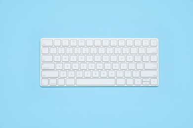 Photo of Modern white wireless keyboard on light blue background, top view