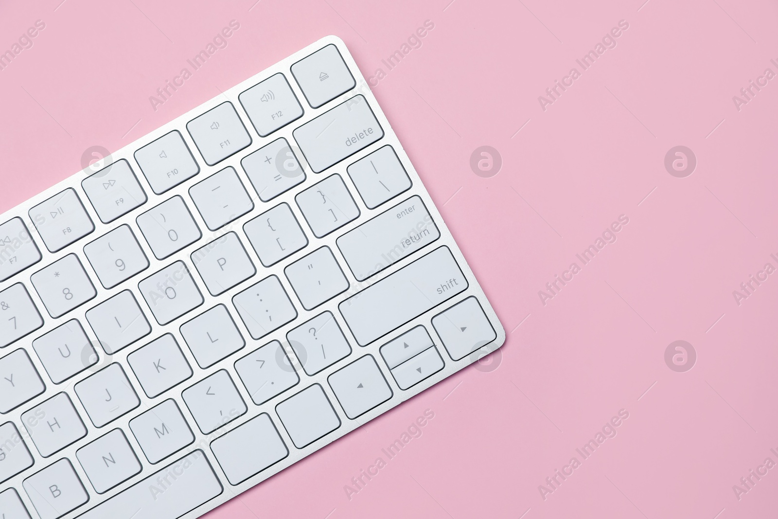 Photo of Modern white wireless keyboard on pink background, top view. Space for text