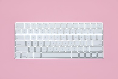 Photo of Modern white wireless keyboard on pink background, top view