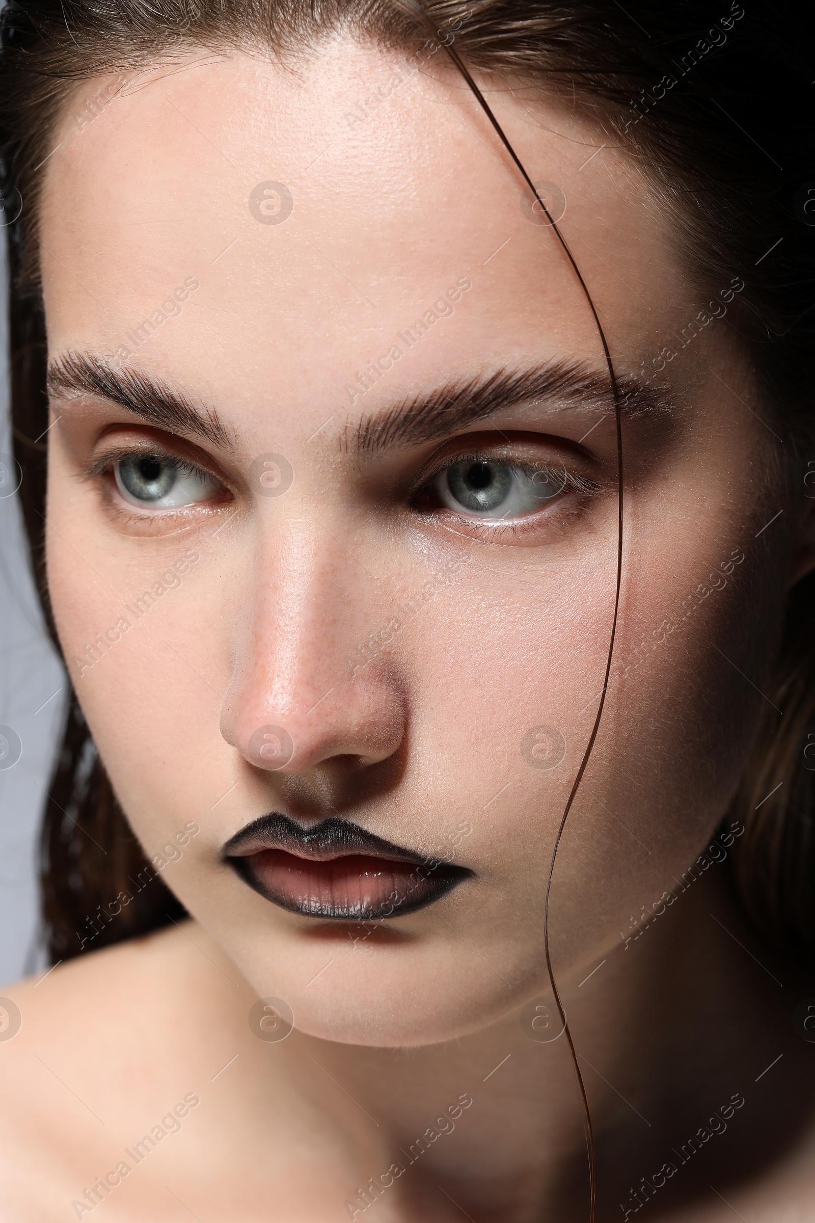 Photo of Beautiful young woman with black lip liner on light grey background, closeup