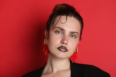 Photo of Beautiful young woman with black lip liner wearing stylish earrings on red background