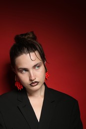 Photo of Beautiful young woman with black lip liner wearing stylish earrings on dark red background