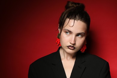 Photo of Beautiful young woman with black lip liner wearing stylish earrings on dark red background, space for text