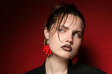 Photo of Beautiful young woman with black lip liner wearing stylish earrings on dark red background