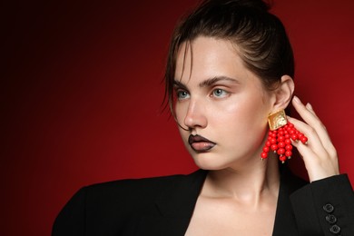 Photo of Beautiful young woman with black lip liner wearing stylish earrings on dark red background, space for text