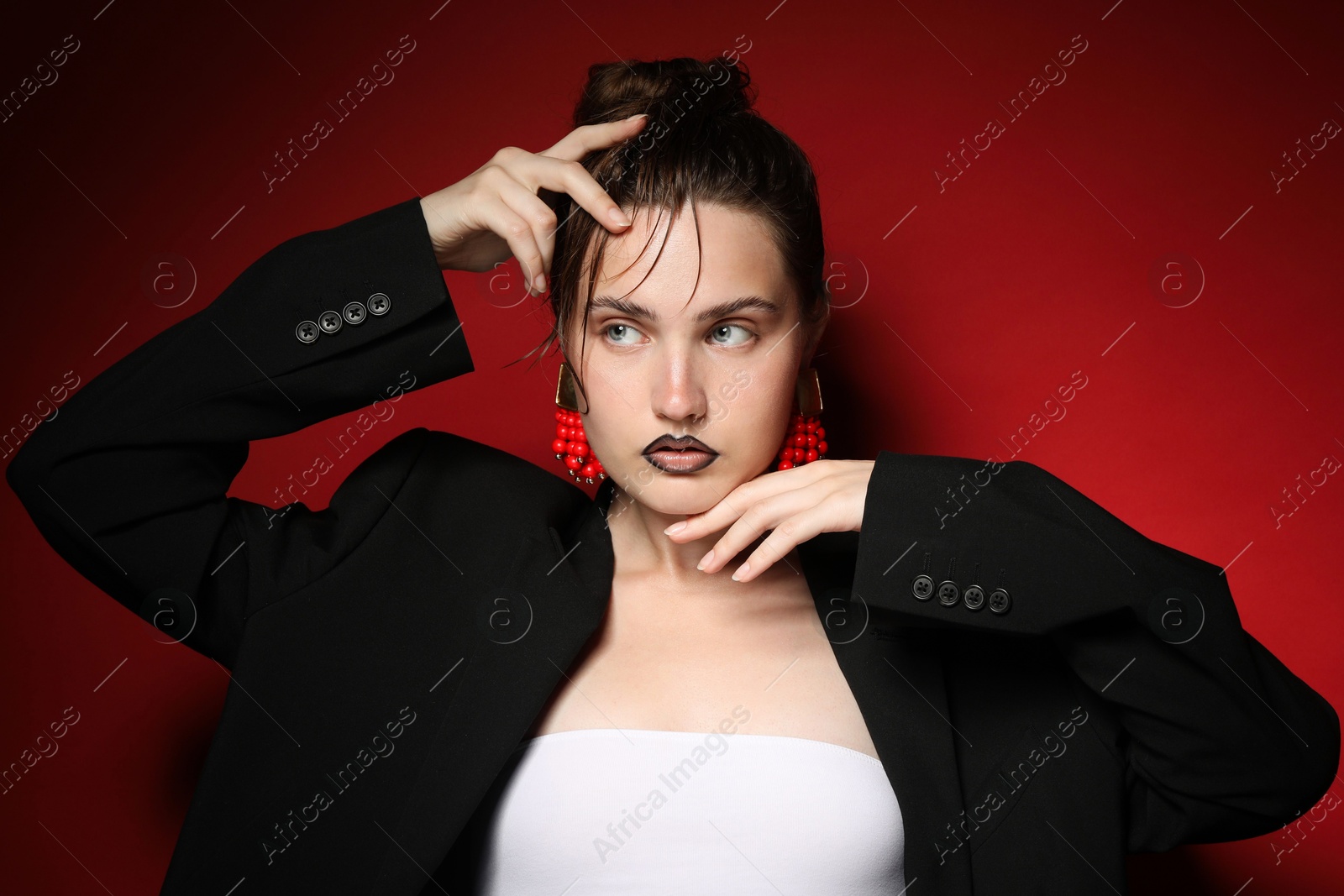 Beautiful young woman with black lip liner wearing stylish earrings on dark red background Photo of Beautiful young woman with black lip liner wearing stylish earrings on dark red background