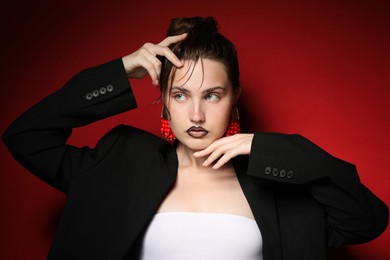 Photo of Beautiful young woman with black lip liner wearing stylish earrings on dark red background