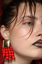 Photo of Beautiful young woman with black lip liner wearing stylish earrings on dark red background, closeup