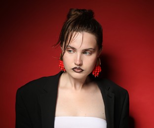 Photo of Beautiful young woman with black lip liner wearing stylish earrings on dark red background