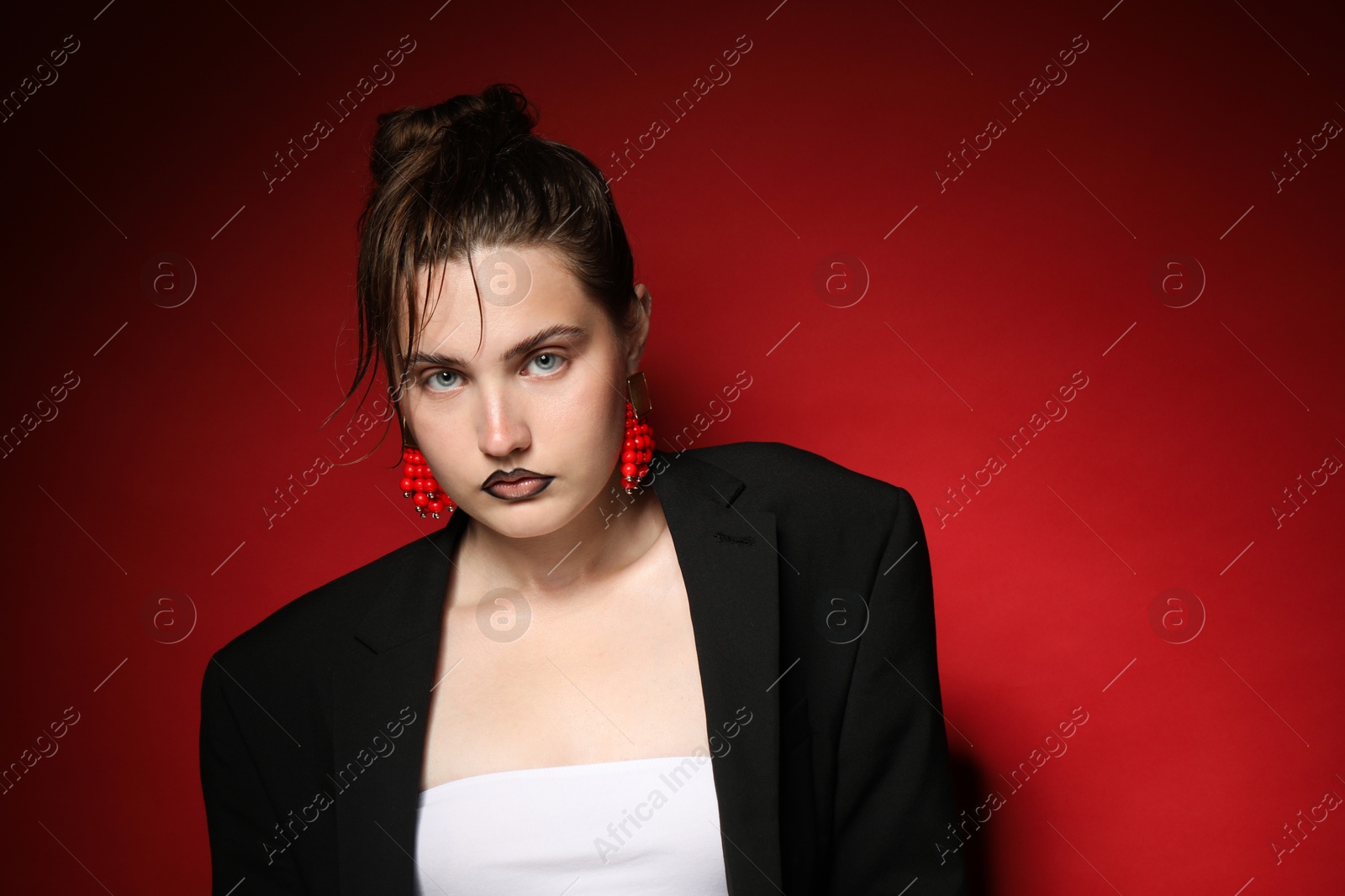 Beautiful young woman with black lip liner wearing stylish earrings on dark red background, space for text Photo of Beautiful young woman with black lip liner wearing stylish earrings on dark red background, space for text