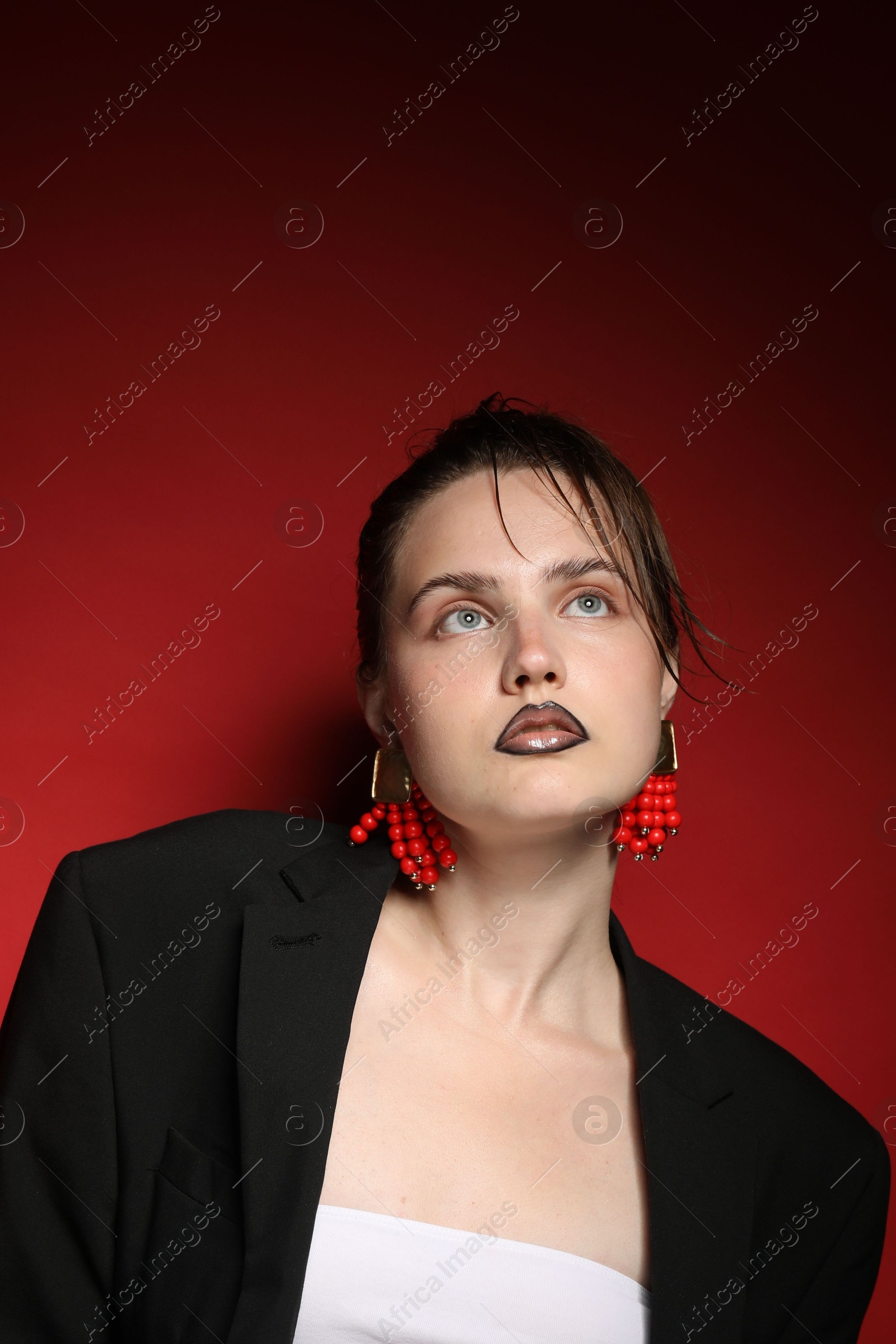 Beautiful young woman with black lip liner wearing stylish earrings on dark red background Photo of Beautiful young woman with black lip liner wearing stylish earrings on dark red background