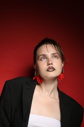 Photo of Beautiful young woman with black lip liner wearing stylish earrings on dark red background