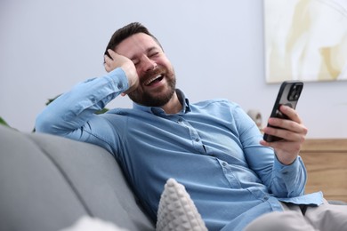 Photo of Man with smartphone laughing on sofa at home